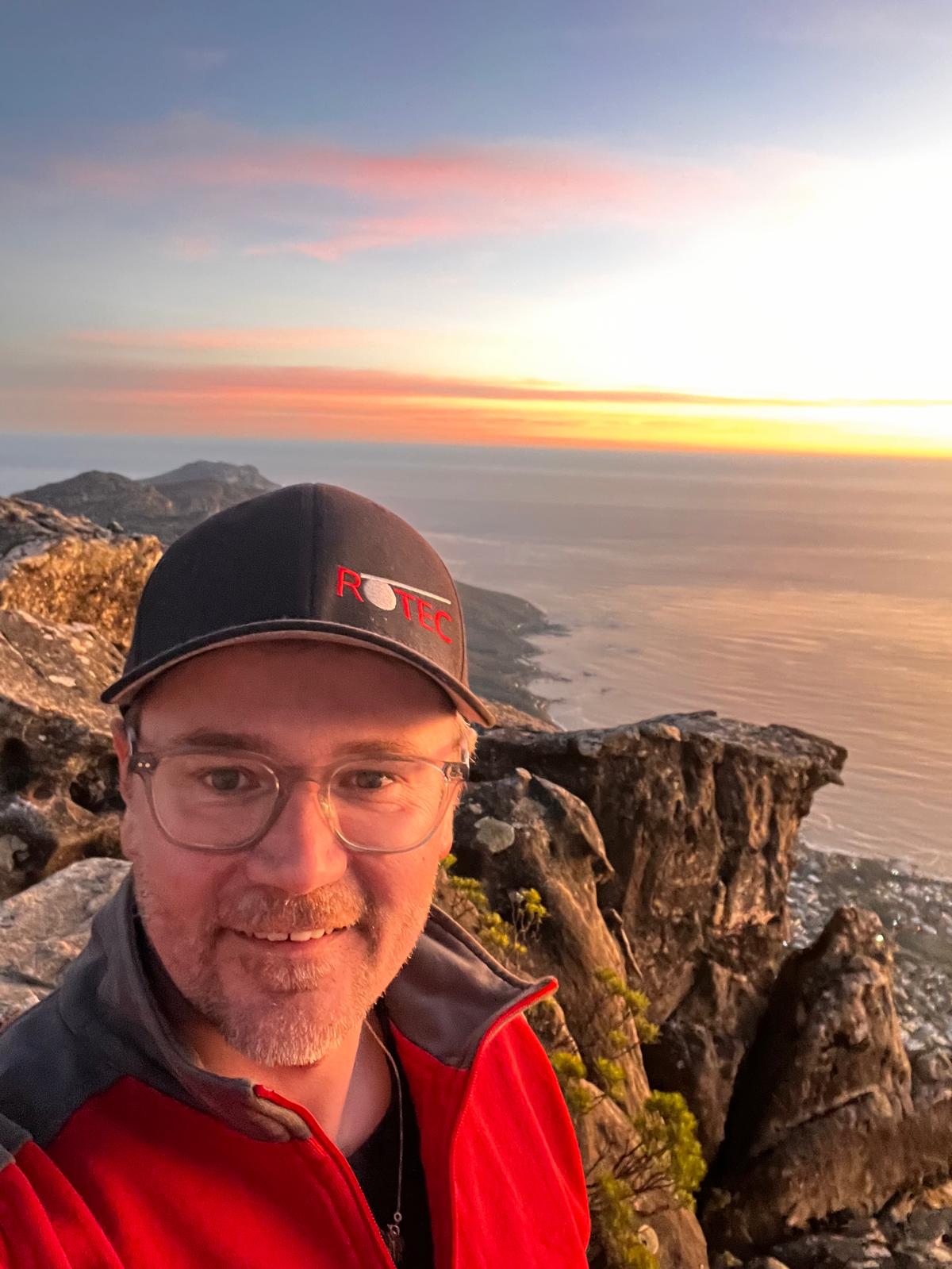 Marcus Liebscher beim Einsatz in Südafrika. ROTEC-Mitarbeiter Marcus Liebscher bei der Zugseilprüfung am Tafelberg mit Felsen und Meer im Hintergrund.