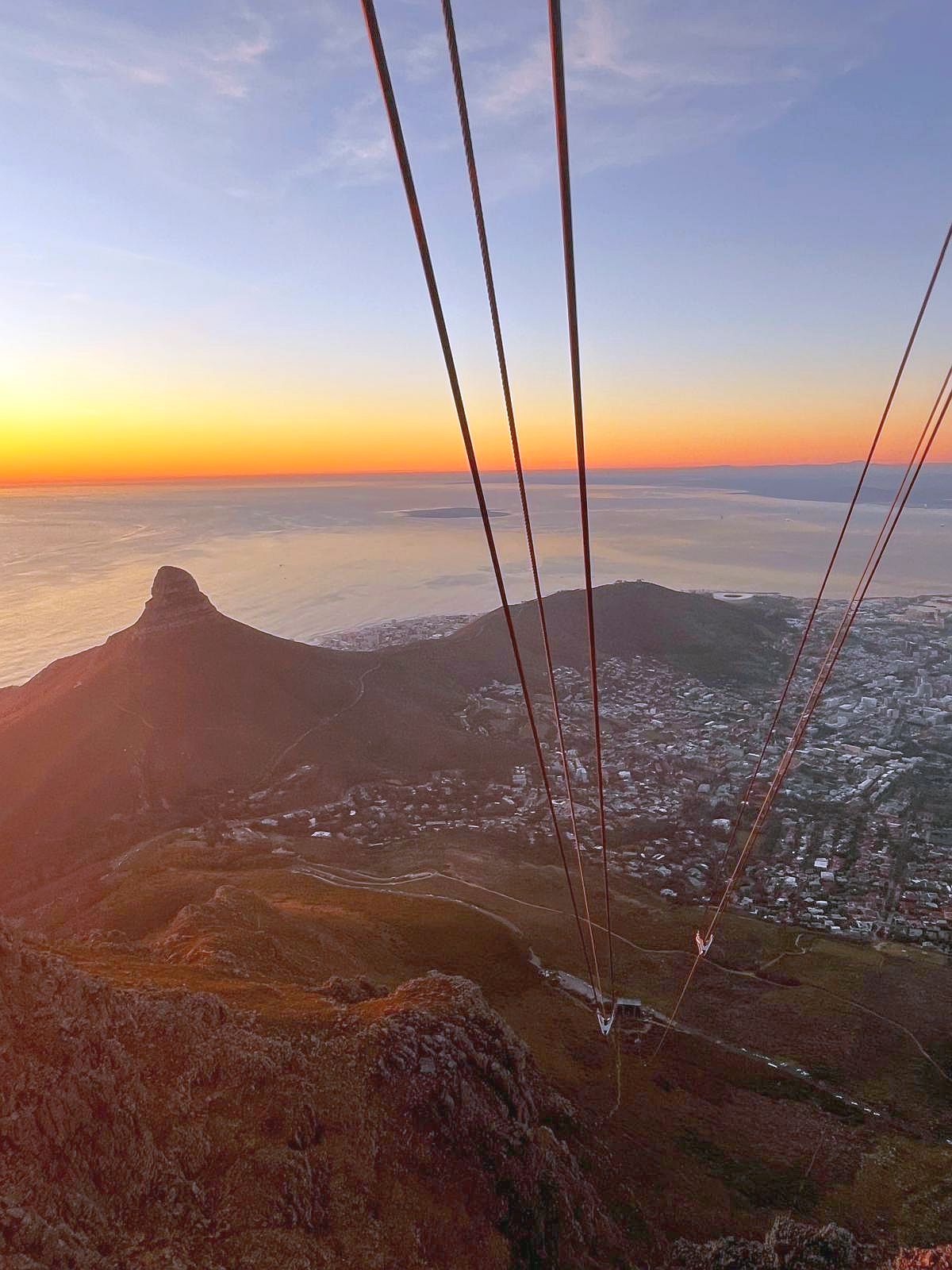 Kapstadt bei Sonnenuntergang vom Tafelberg. Blick von der Seilbahnstation auf dem Tafelberg über Kapstadt in der Abenddämmerung mit Seilbahnseilen.