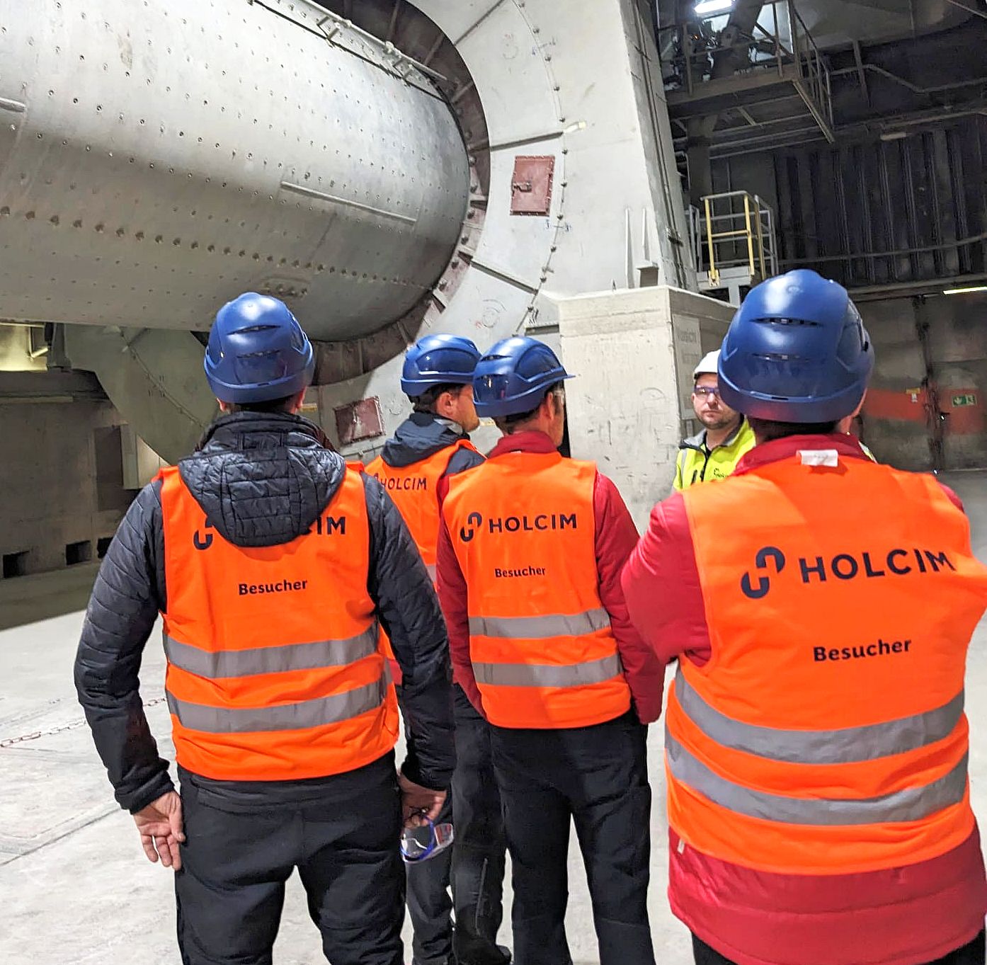 ROTEC-Team mit orangen Sicherheitswesten und Helmen in der Werkshalle von Holcim Zement