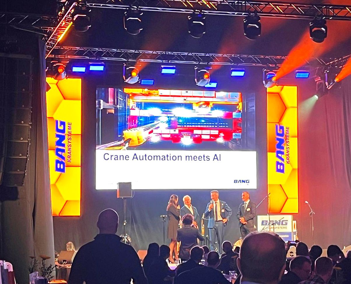 Beleuchtete Bühne mit Sprechern und Moderatoren, im Vordergrund sitzendes Publikum