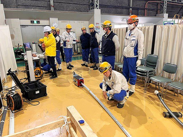Technicians wearing hard hats in a factory hall during practical instruction on a rope testing device.