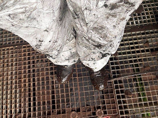 A view from above of the legs of a technician in a protective suit completely smeared with black grease.